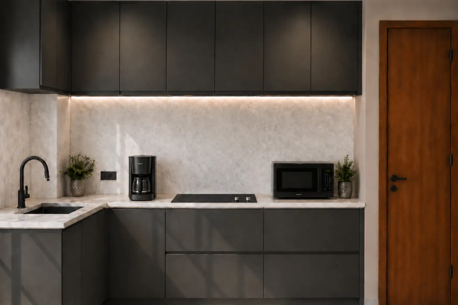 Modern L-shaped kitchen with dark matte cabinets, gray countertops, under-cabinet lighting, and a door on the right.