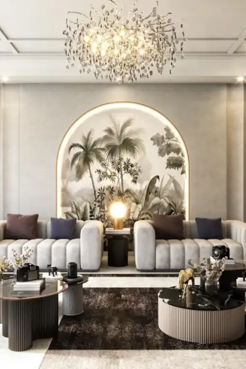 Project Prerna Luxurious living room with white curved sofas, a tropical mural behind an arch, and a crystal chandelier.